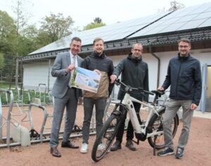 Oberbürgermeister Erik Pauly (von links), Manuel Zimmermann und Jens Fröhlich vom GVV Umweltbüro sowie Heiko Kastorf vom Hochbauamt freuen sich über die Auszeichnung der Landesenergieagentur. Die Zertifizierung belegt, dass die Stadtverwaltung Donaueschingen auf dem Weg hin zur Klimaneutralität bis 2040 auf einem guten Weg ist. Dazu tragen auch die neue PV-Anlage beim Parkschwimmbad im Hintergrund sowie zwei komfortable E-Bikes für Mitarbeiter bei.